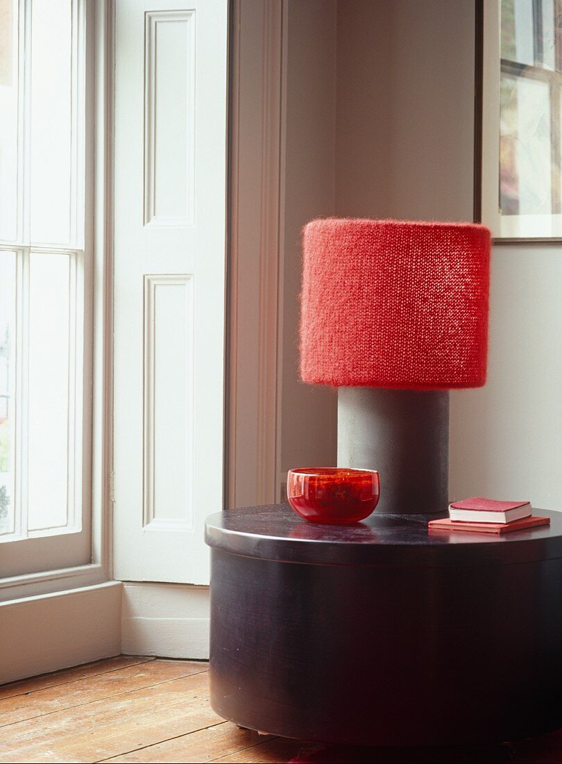 Lamp with red shade and red ornaments on modern table next to terrace door and white wall panel