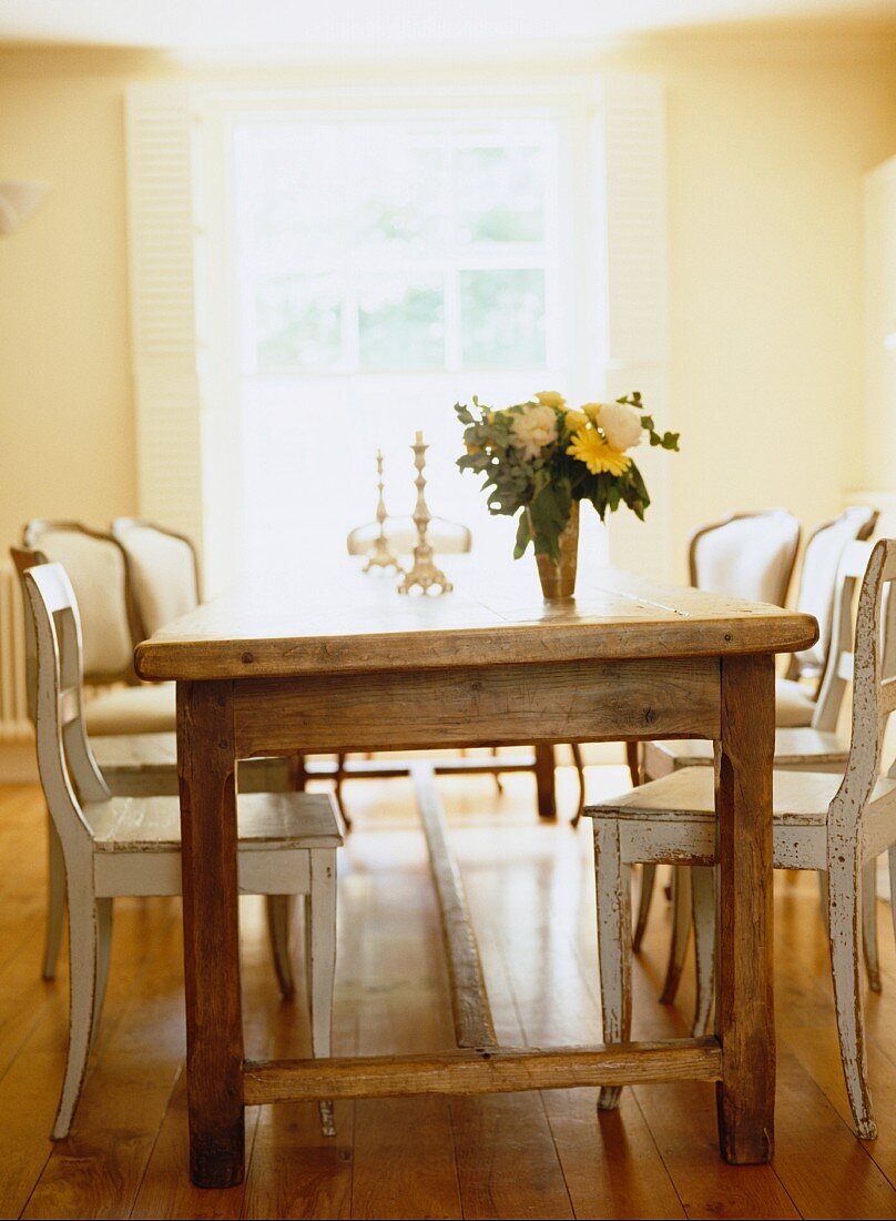 Rustikaler Esstisch aus naturbelassenem Holz mit gemischten Stühlen und Blumenstrauss