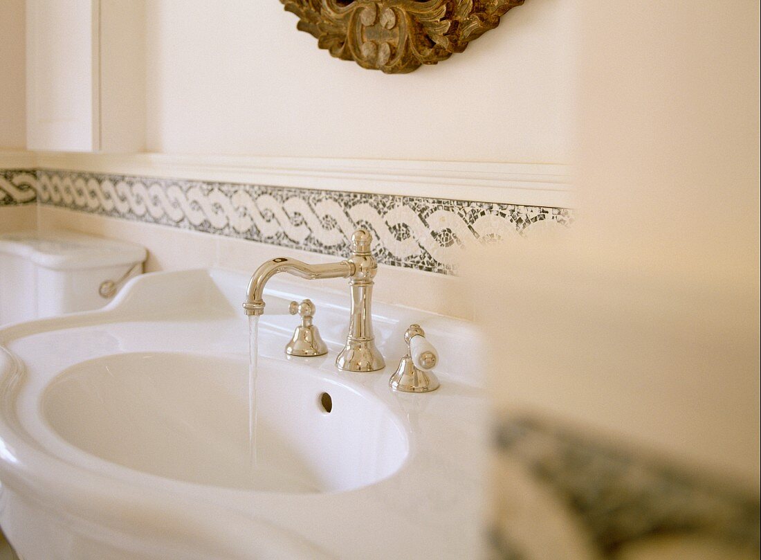Curved sink with silver, antique-style tap fittings against wall with plaited border