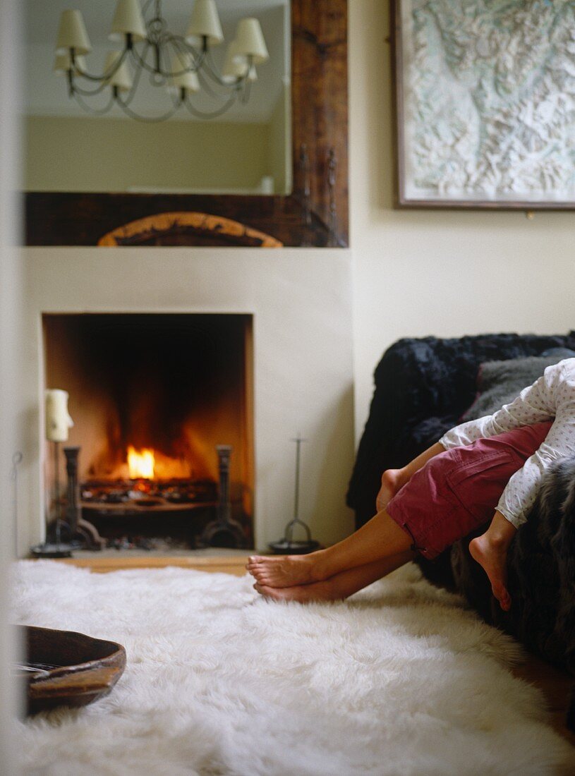 Large mirror above fire in fireplace and feet on white fur rug