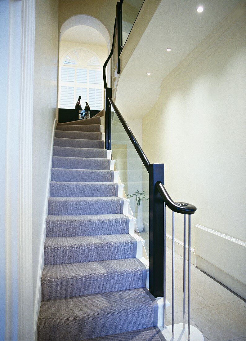 Grey runner and glass balustrade in stairwell with view of arched window
