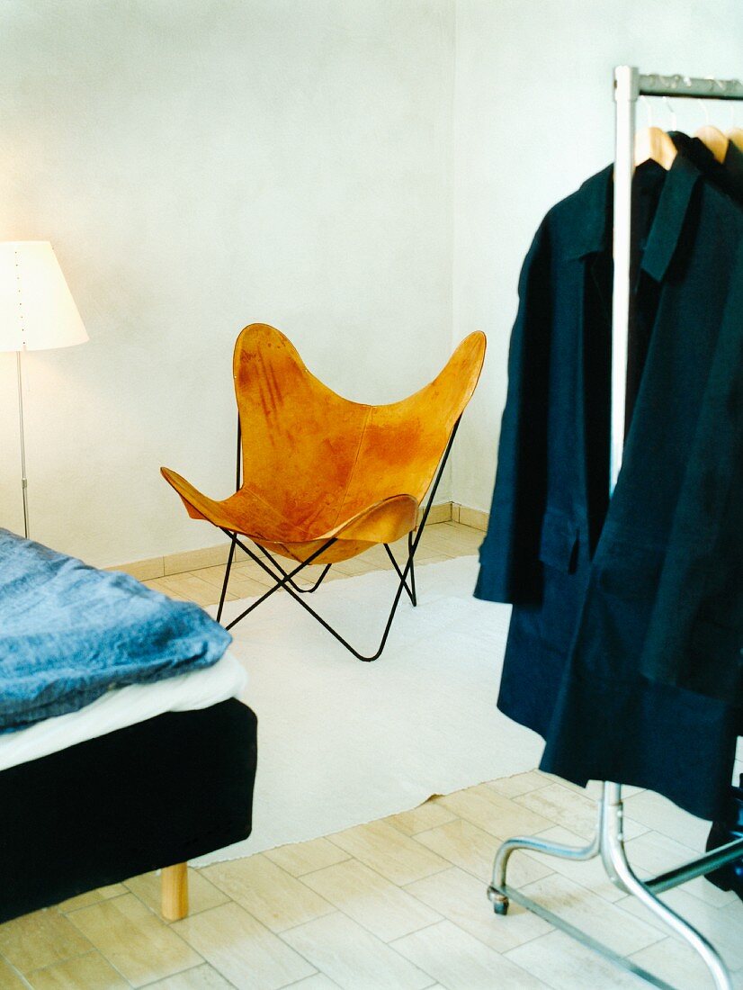 Designerstuhl vor Bett und Kleiderstange mit Kleidung