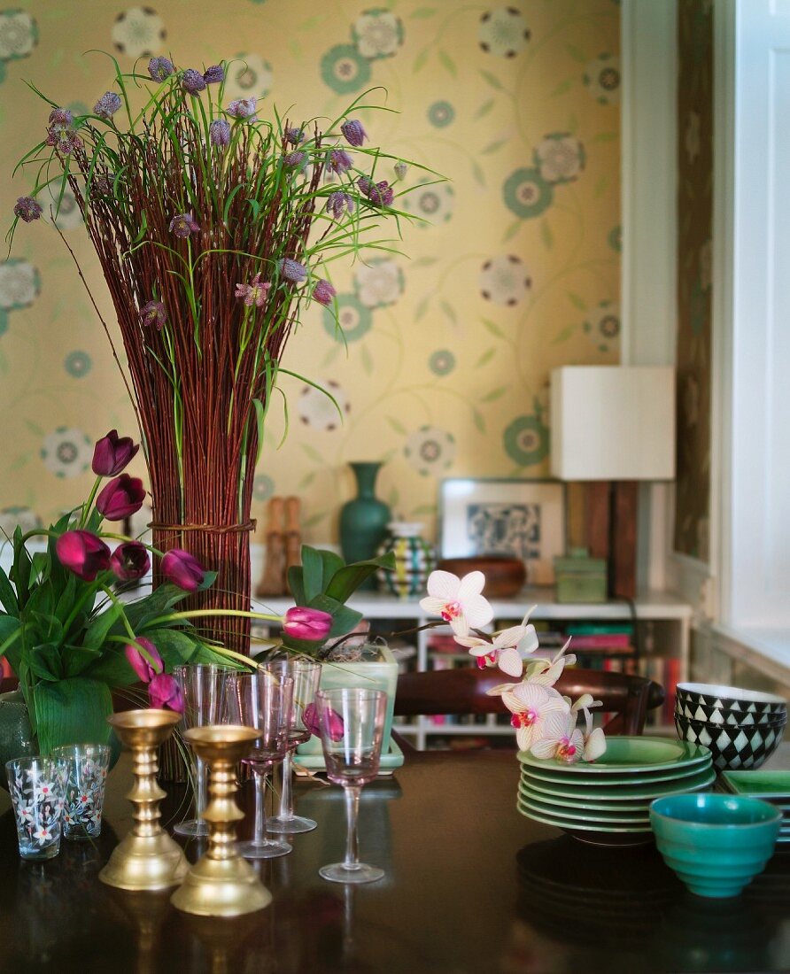 Gläser und Schalen vor Blumensträussen auf Tisch