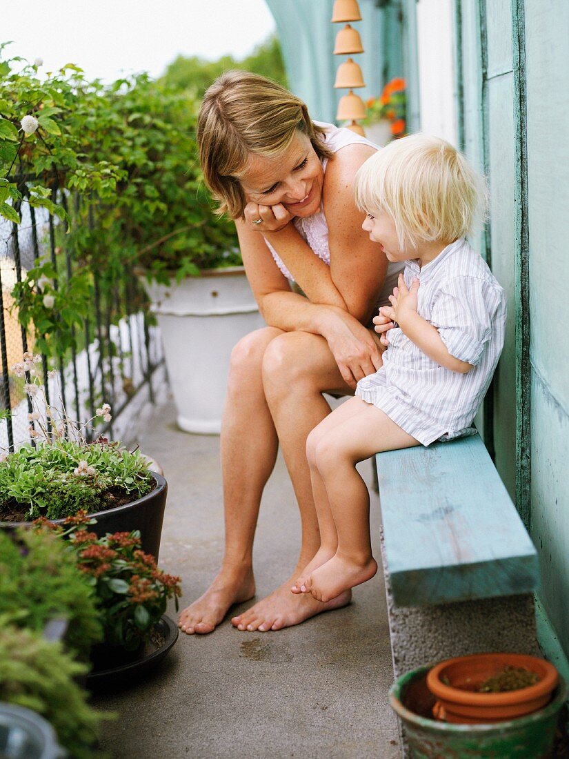 Mutter und Sohn auf Holzbank und Blumentöpfe auf Balkon