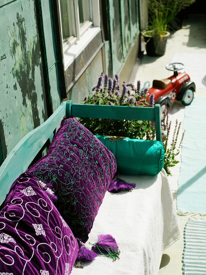 Kissen mit violettem Samtbezug auf sonnenbeschienene Holzbank