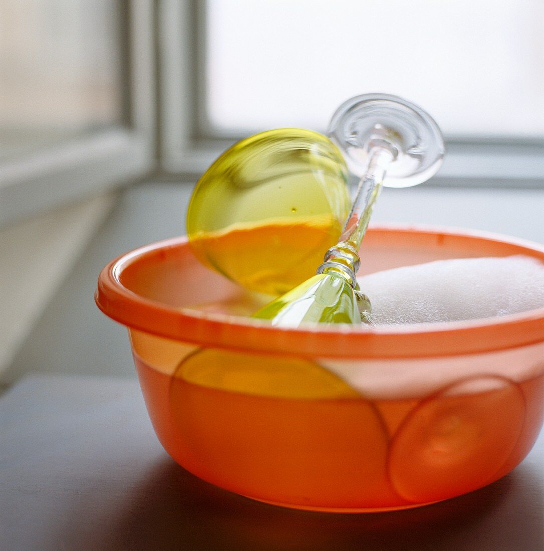 Colored stemware being washed in an orange plastic bowl