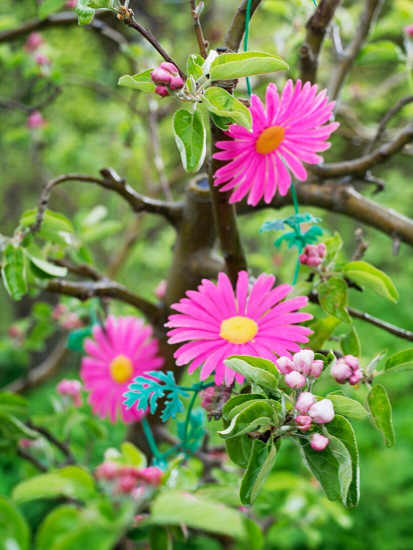 Pinkfarbene Plastikblumen um Blütenzweig gewickelt