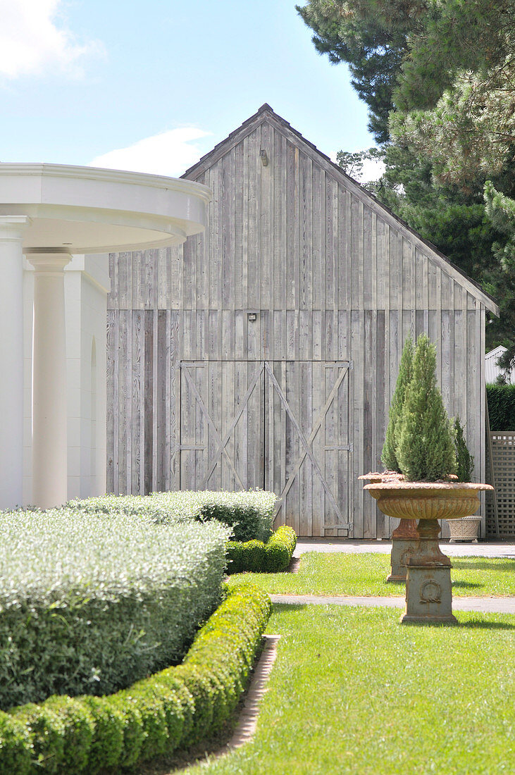 Manicured garden with cyprus trees in antique planters in front of old barn