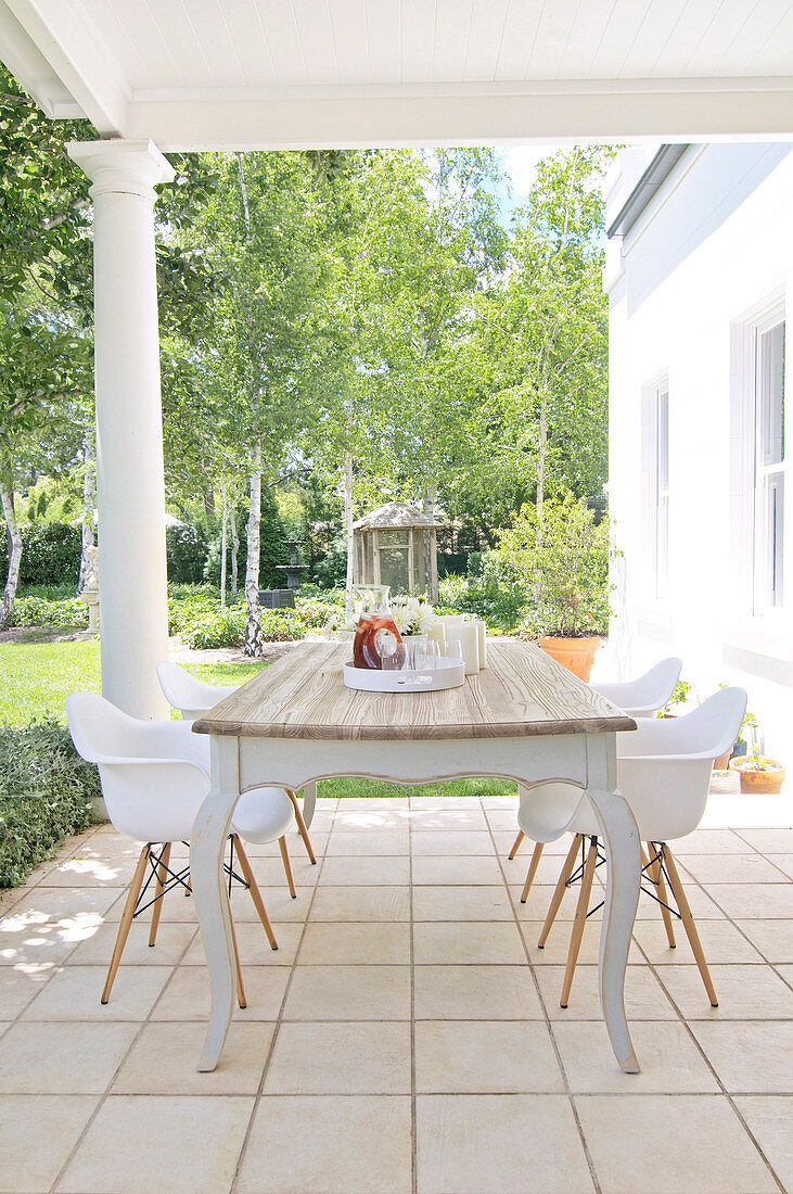 Rustic table with shell chairs on roofed, colonial-style terrace with view of garden