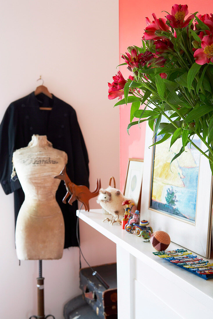 Tailor's dummy and dress hanging up in corner next to bouquet on shelf