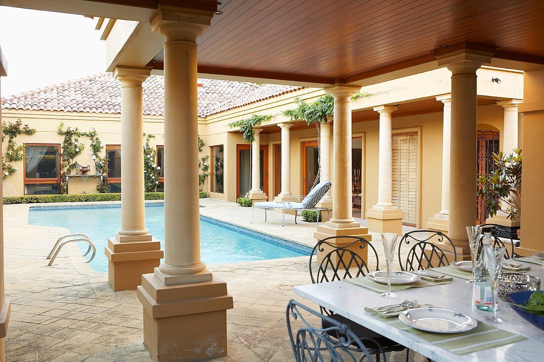 Set table on roofed terrace with colonnade and pool belonging to mansion
