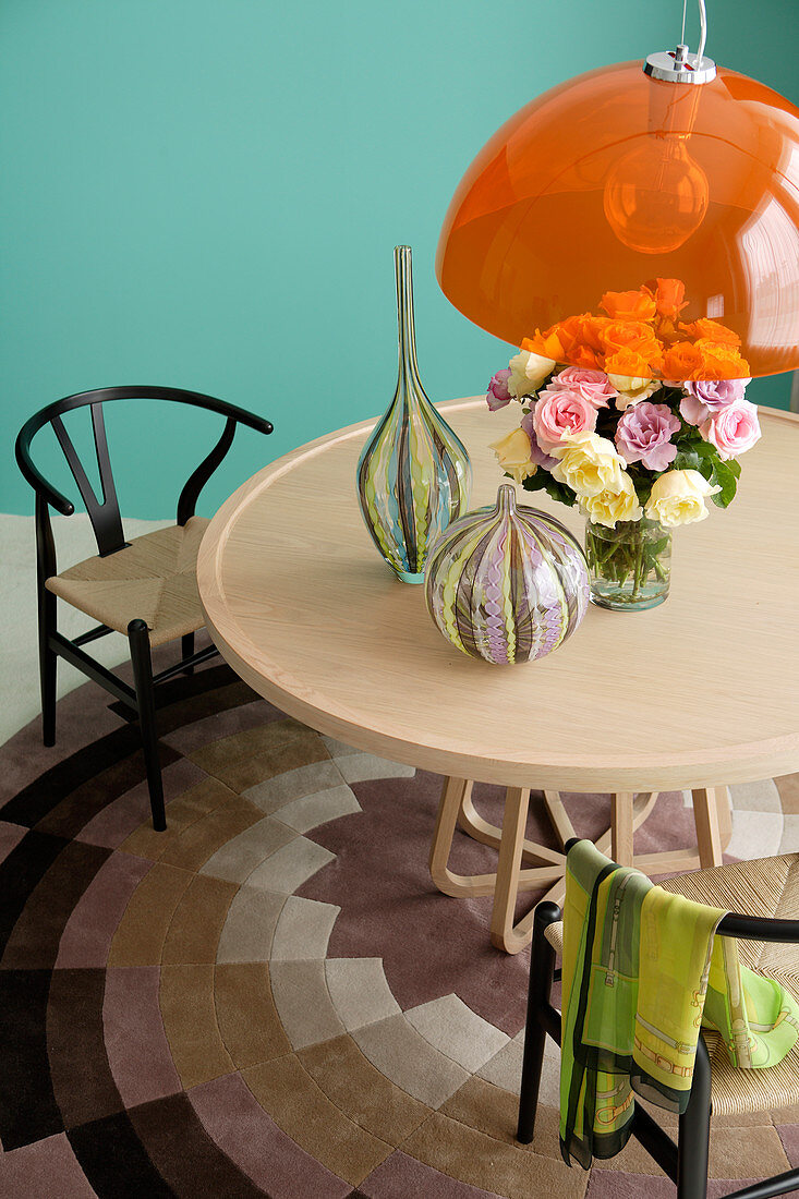Orange pendant lamp above round wooden table and rug in front of turquoise wall