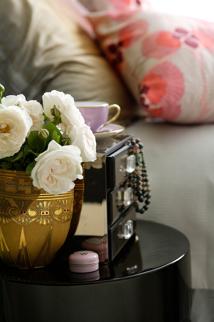 weiße Rosen in Vase aus Messing neben Kästchen mit Schmuck in Schublade auf schwarzem Beistelltisch