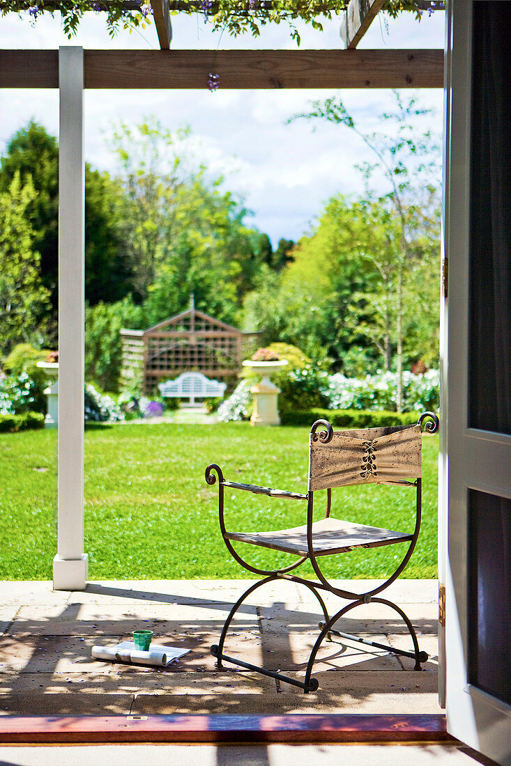 Leichter Stuhl aus Metall und Leinen auf Terrasse mit Blick in sonnenbeschienen Garten