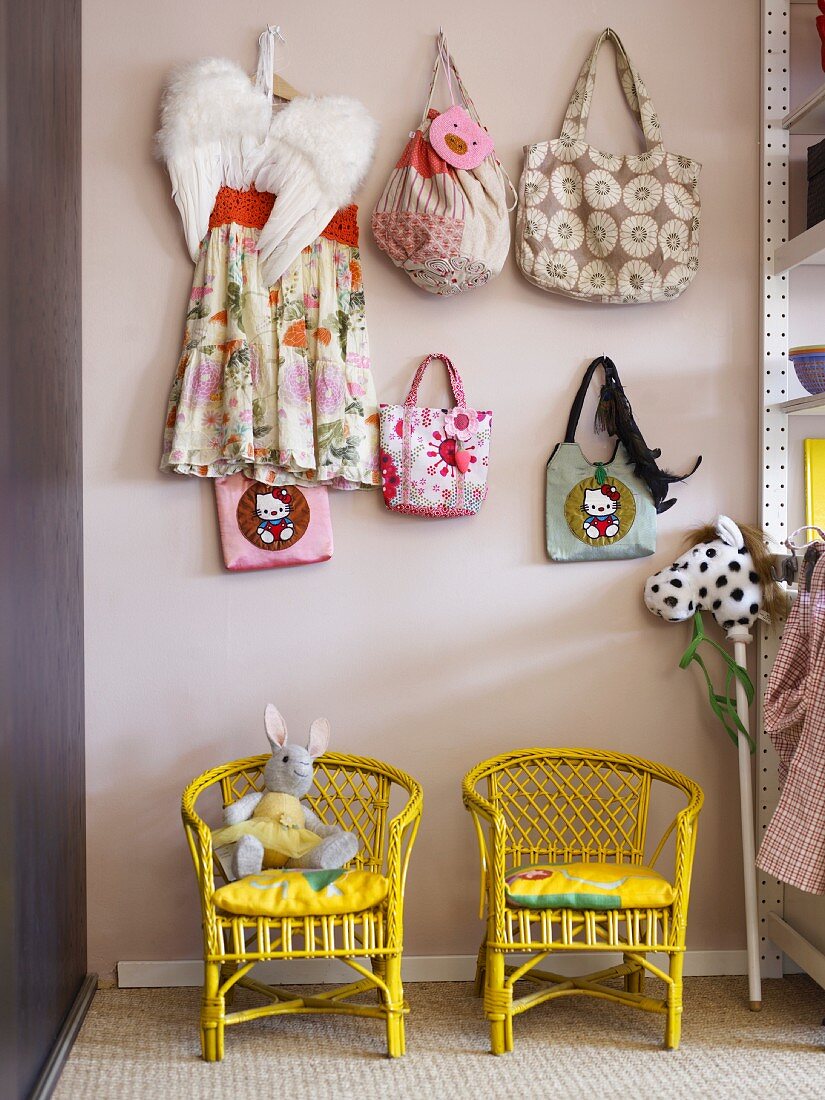 Yellow, wicker children's chairs with bags hanging on wall hooks above