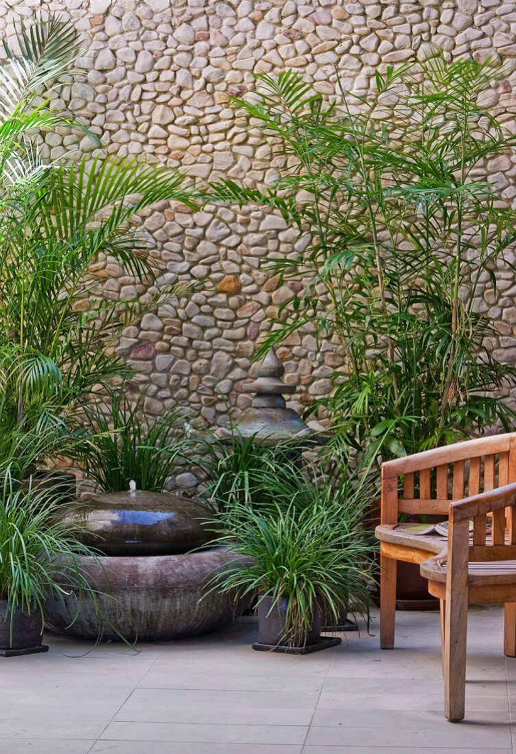 Fountain and foliage plants against stone wall