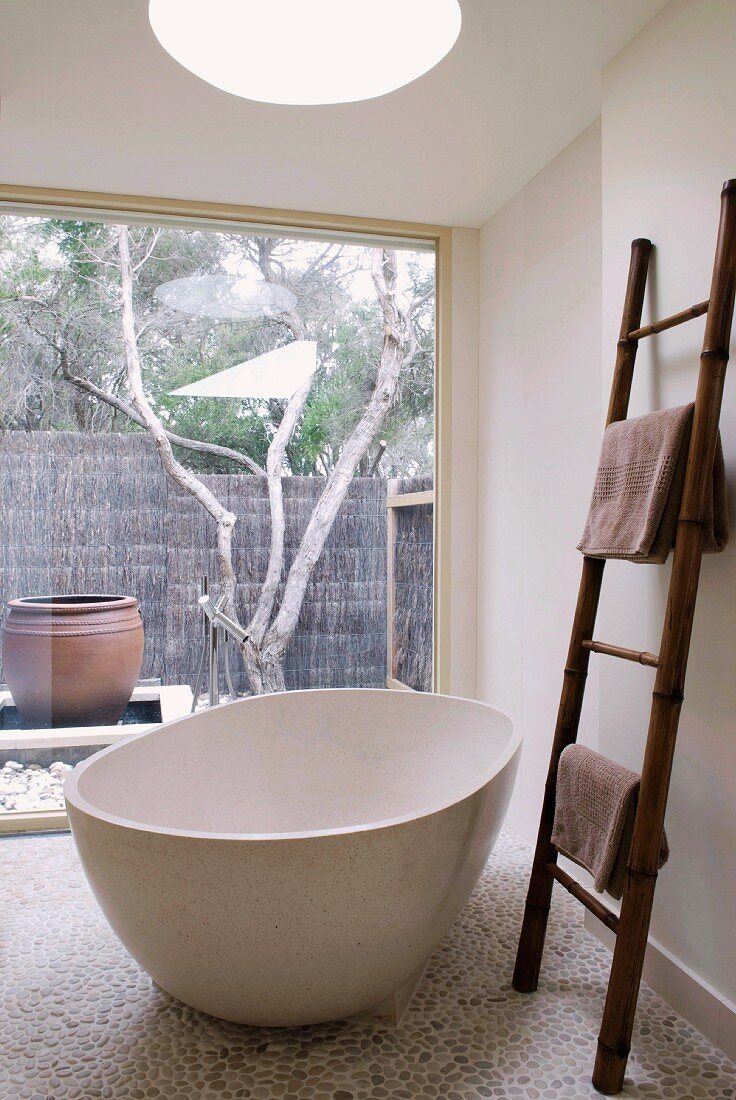 Frei stehende Badewanne und eine Leiter als Handtuchhalter in einem Badezimmer mit Glasfront