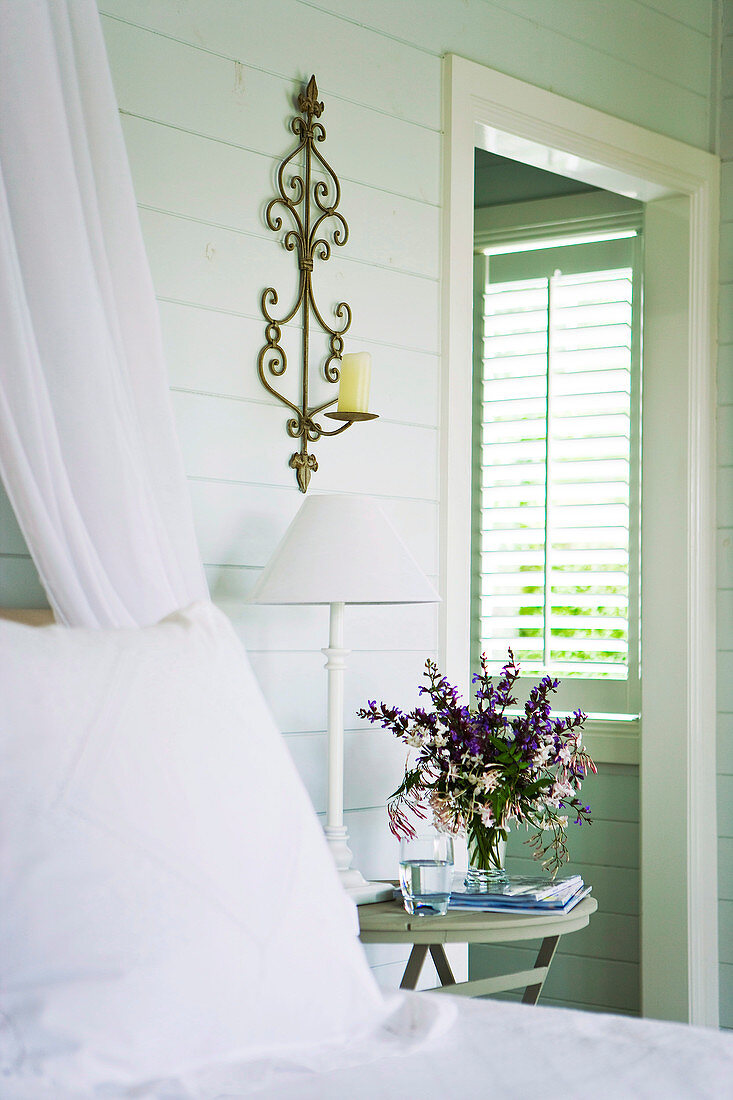 Ländlicher Schlafraum mit Blumenstrauss auf Nachttisch und Blick durch offene Tür auf Fenster