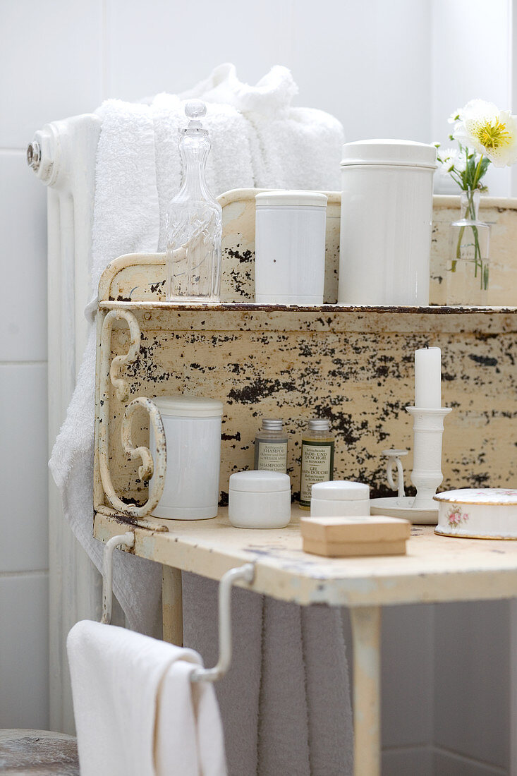 White containers on peeling, vintage metal washstand and towels on radiator