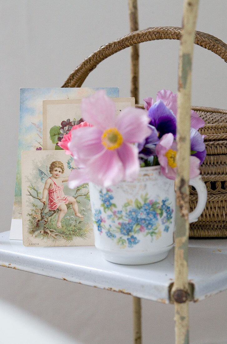 Romantisches Arrangement auf Vintageregal - Anemonen in Blümchenbecher vor nostalgischen Postkarten