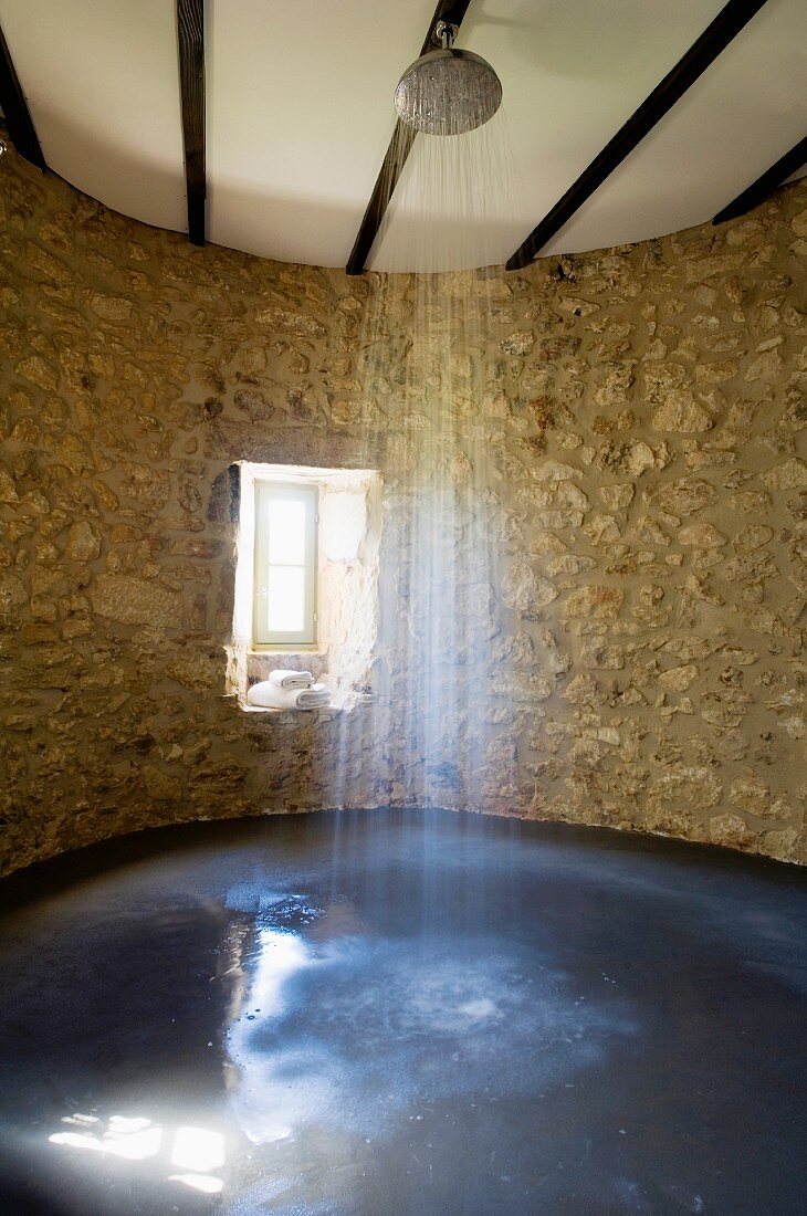 Shower in spacious shower area within curved, old stone wall