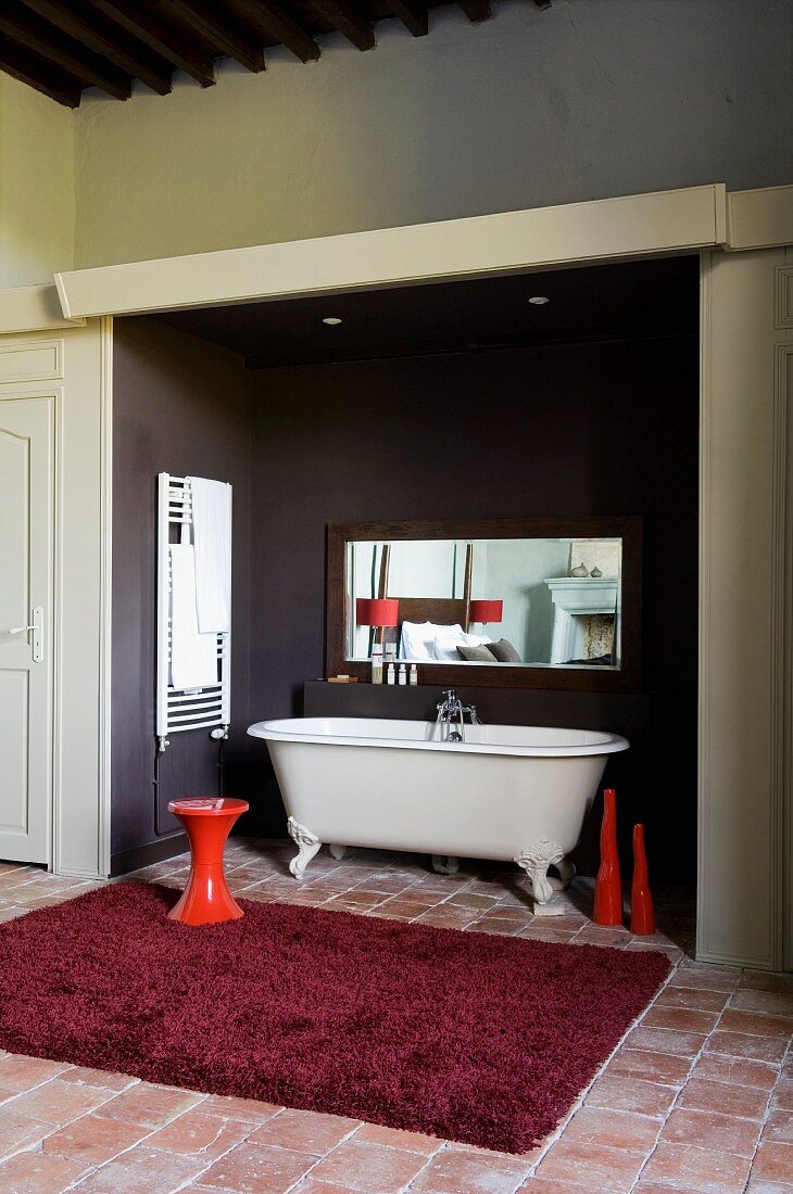 Bordeaux-red rug in front of free-standing vintage bathtub in niche painted dark grey