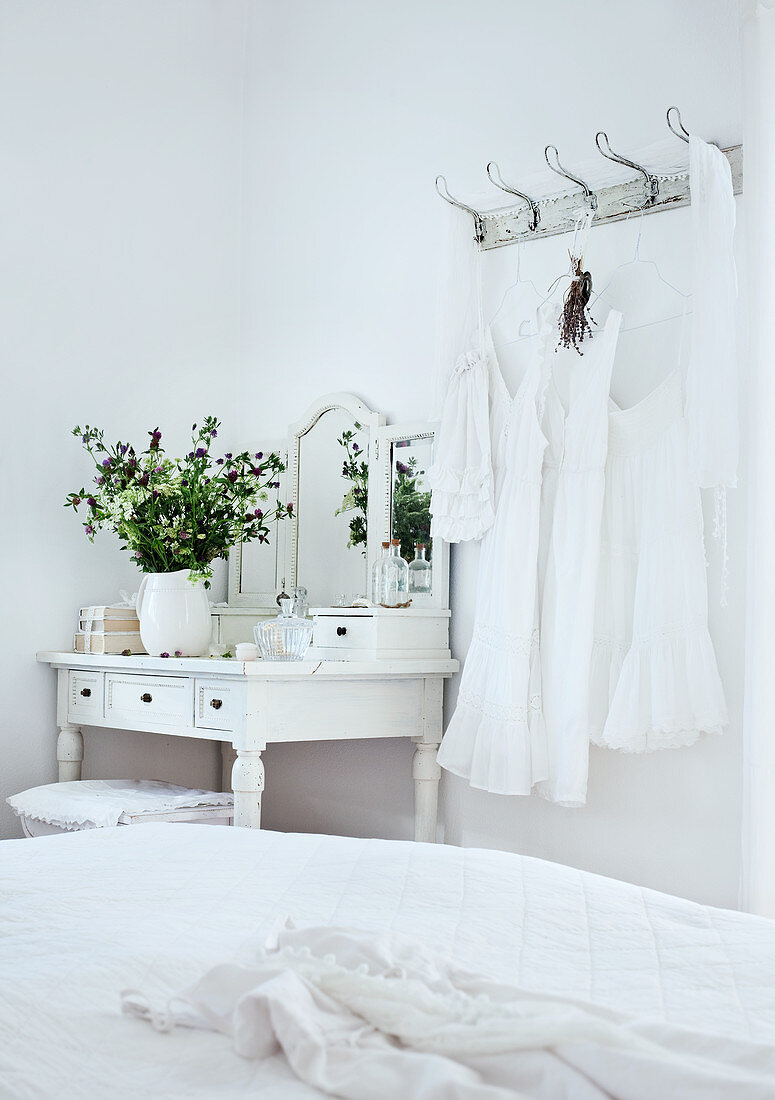 Lacy dresses hanging on wall hooks next to white, rustic dressing table in corner of bedroom