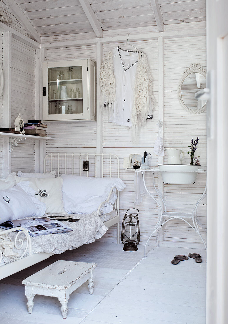 Weiß gestrichenes Zimmer im Holzhaus mit Einzelbett aus Metall und Waschtisch im Vintagestil