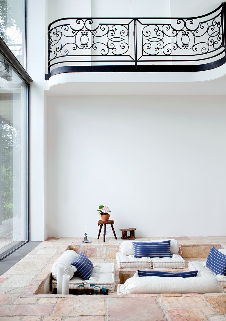 Gemütliche Sitzgrube im steingefliesten Fussboden eines Wohnzimmers mit Fensterfront und Galerie