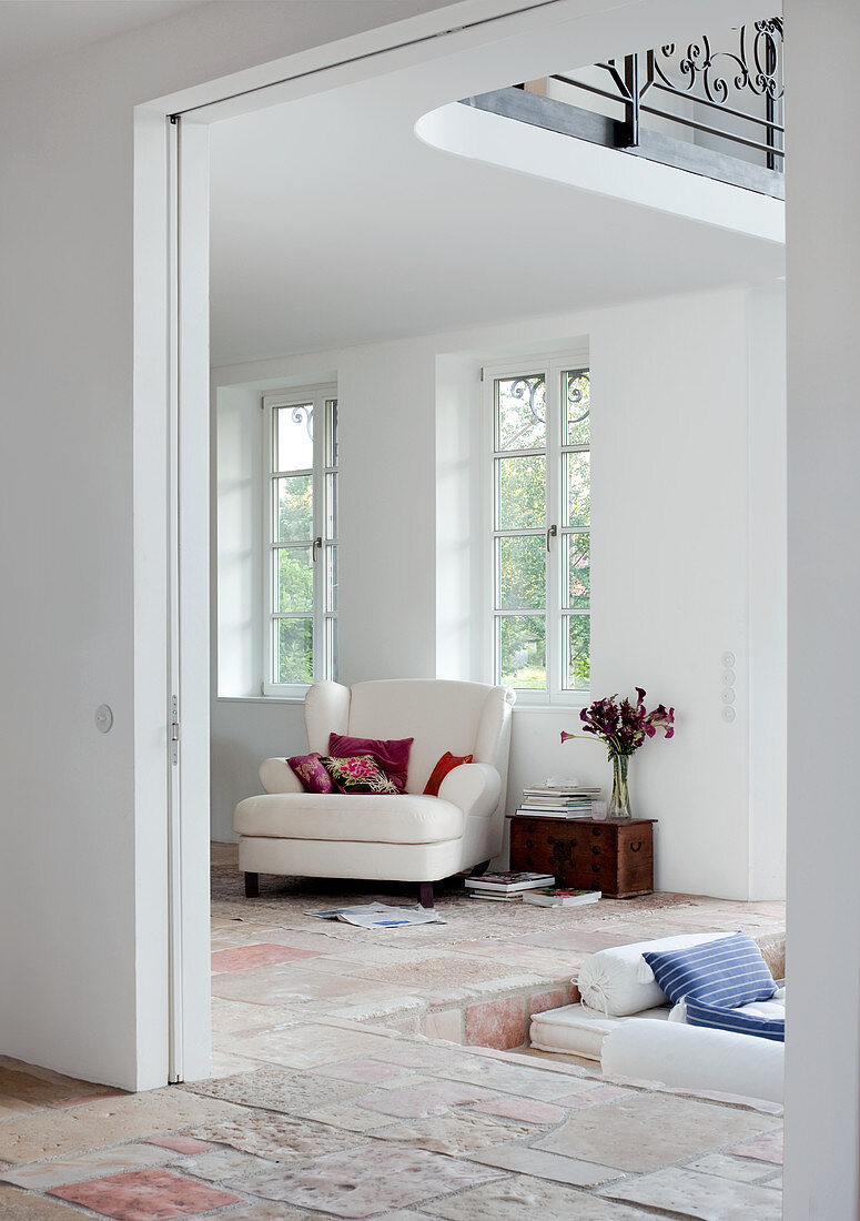 Klassischer, weisser Sessel im Wohnzimmer mit Natursteinboden und Sitzgrube