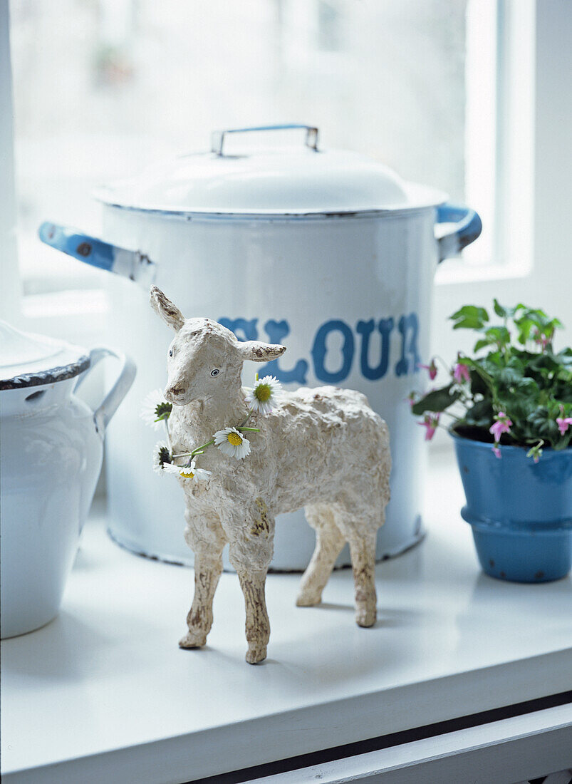 Decorative lamb with daisy chain and enamel pots on a windowsill