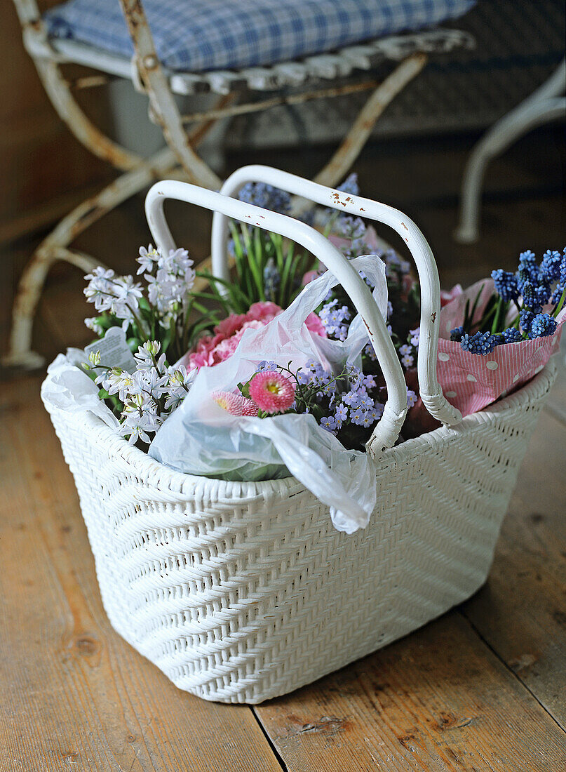 Weißer Korb mit Frühlingsblumen auf Holzboden