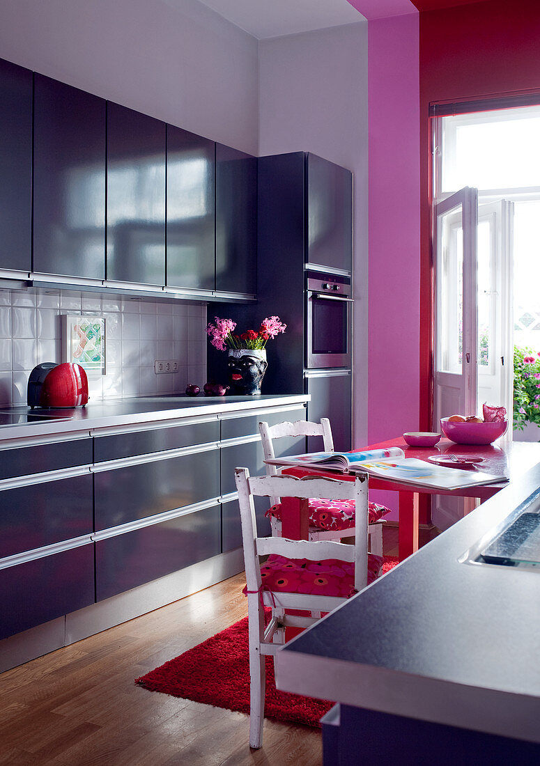 Modern fitted kitchen in muted blue combined with pink and red accents and vintage chairs