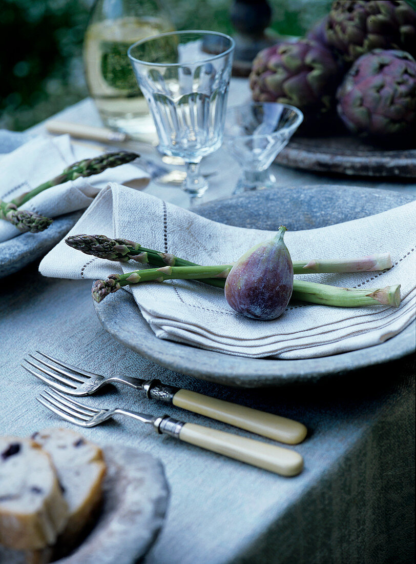 Place setting with fig and green asparagus on linen napkin and rustic stone plate