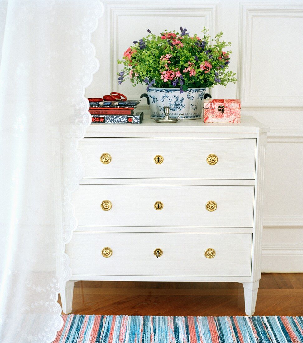 Light curtain in front of white chest of drawers with brass fittings