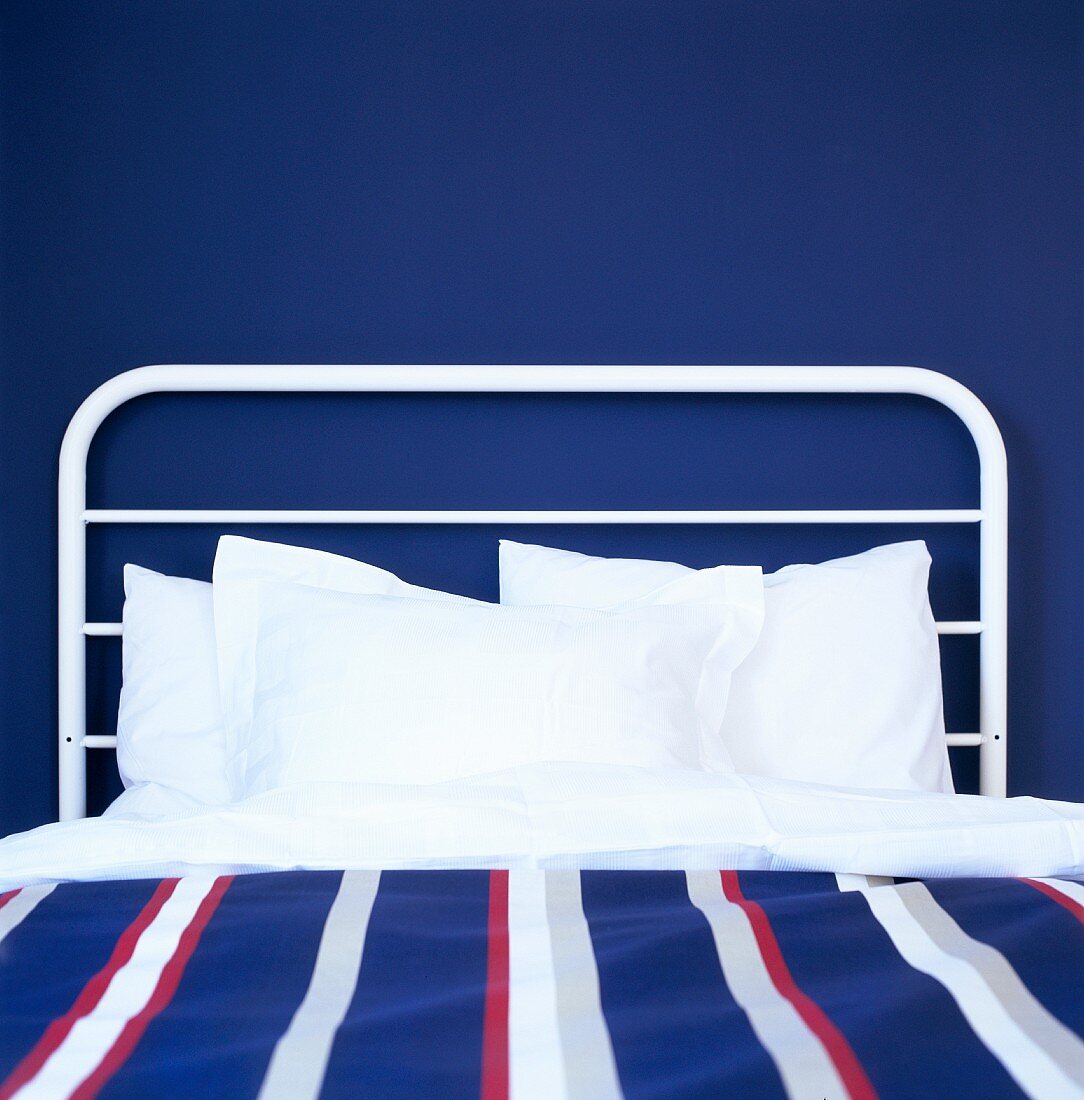 Bed with white metal frame in front of a dark blue wall