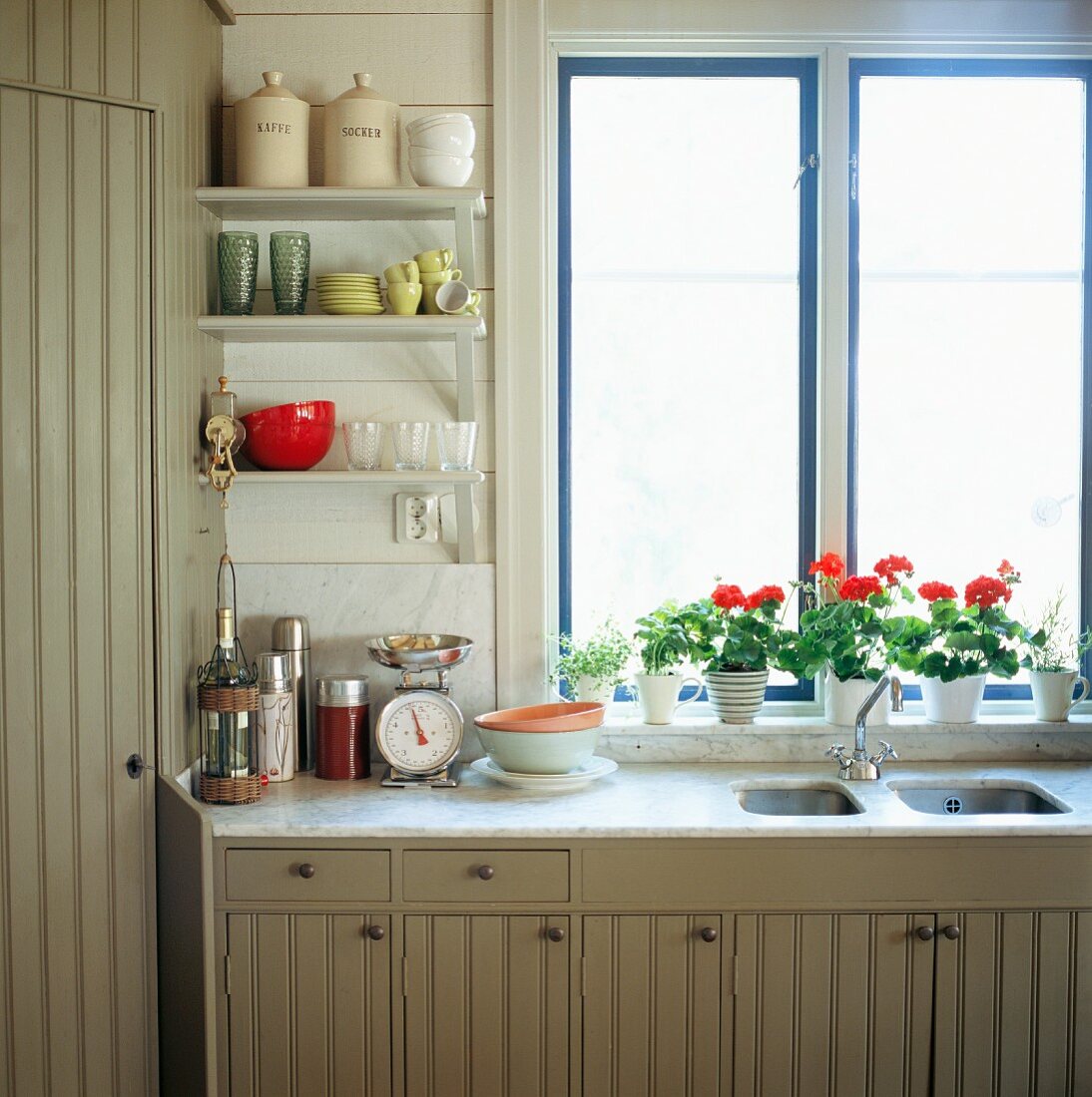 Ländliche Küchenzeile mit hellgrau lackierten Holzfronten vor Fenster