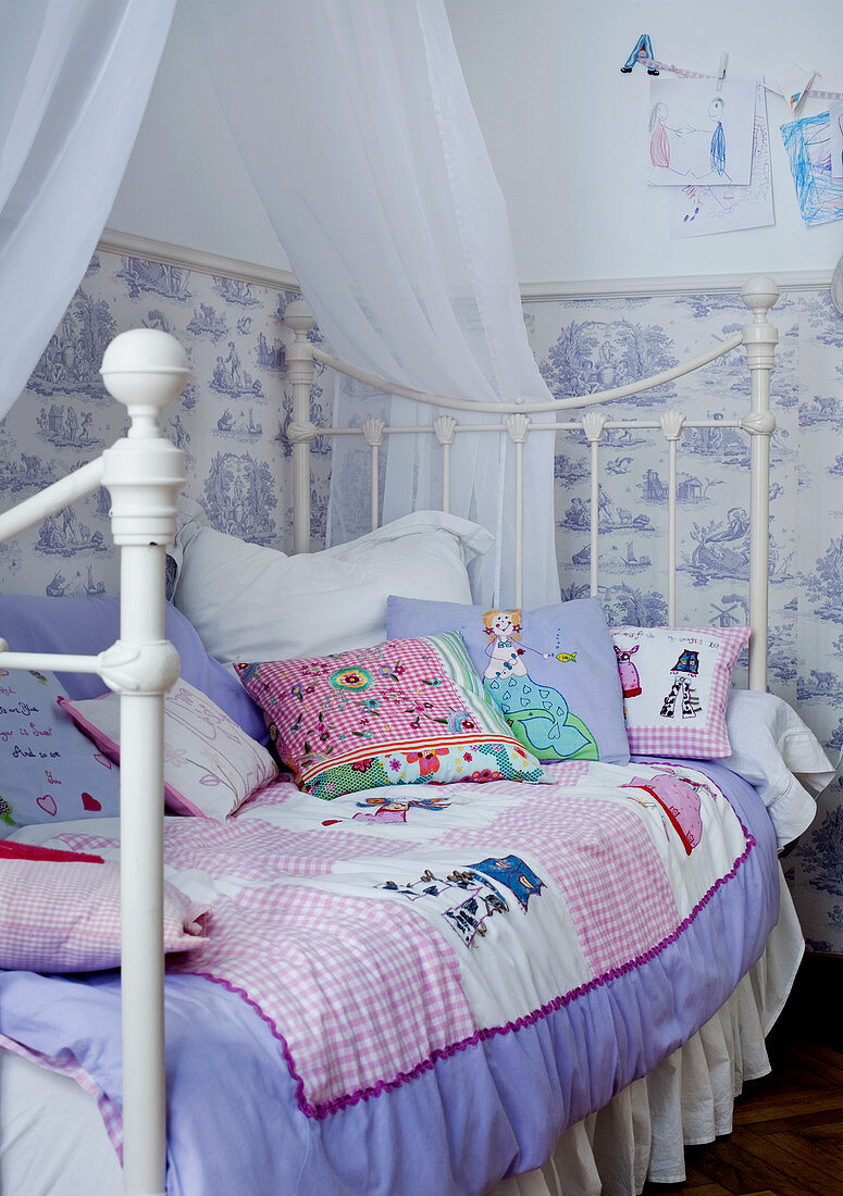 Patchwork quilt on vintage-style canopied bed against wallpapered wall in child's bedroom