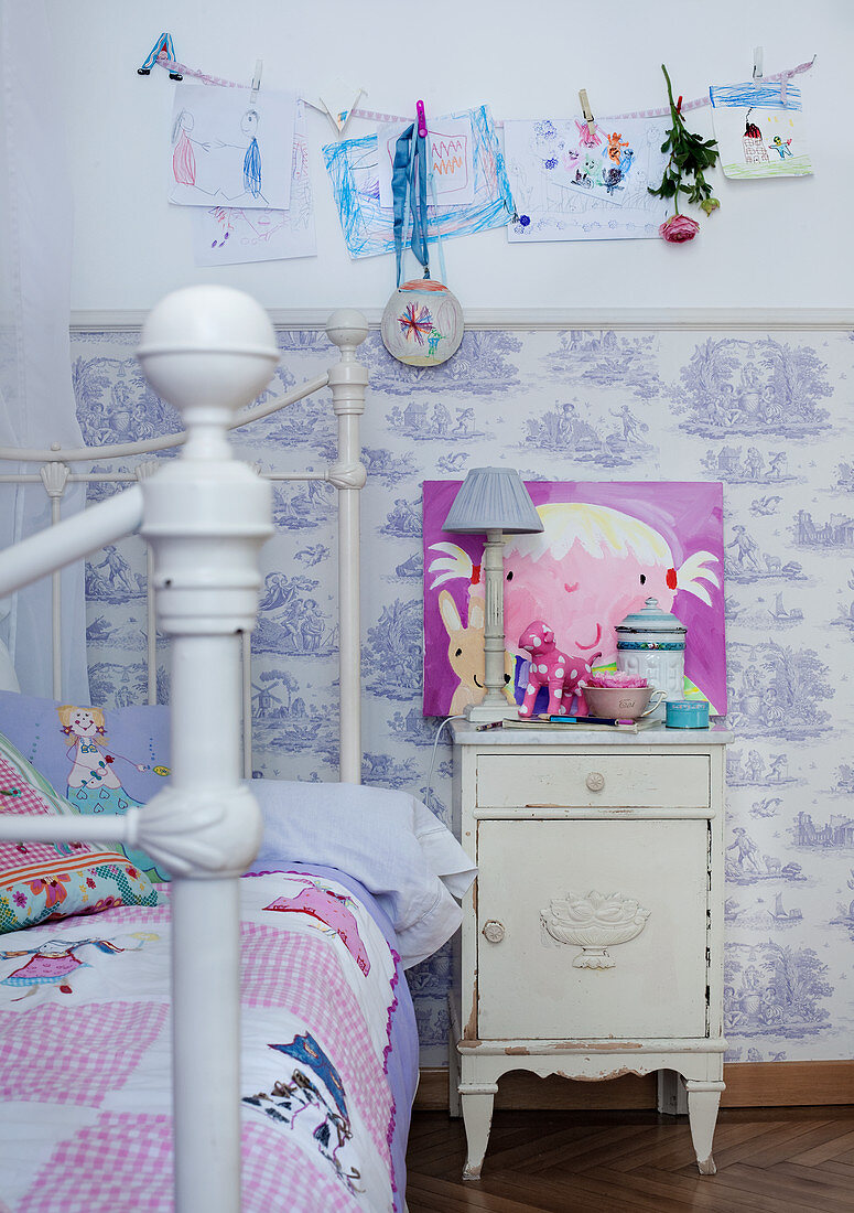 Child's bed with quilt next to rustic bedside cabinet against half-height Toile de Jouy wallpaper