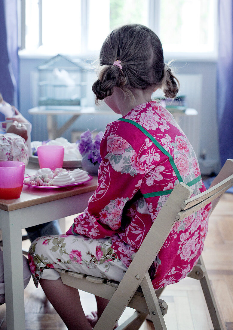Kindergeburtstag - Mädchen sitzt am Tisch vor Süssigkeiten