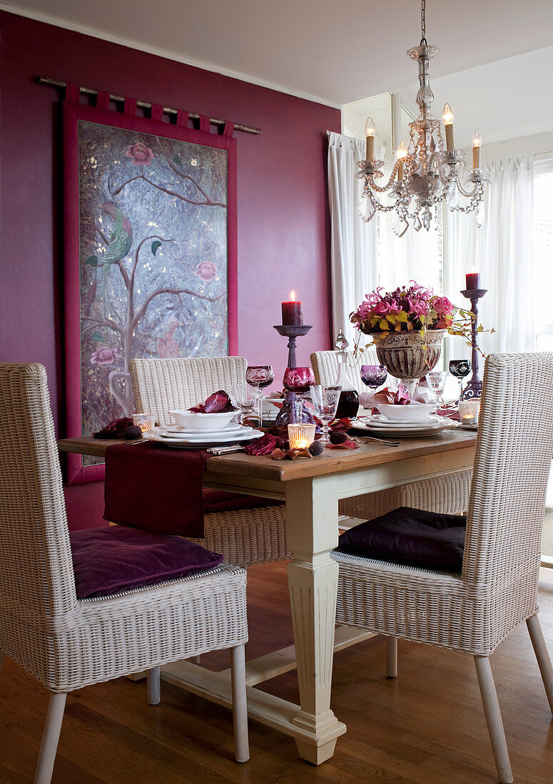 Festively set dining table and wicker chairs in front of tapestry on purple wall