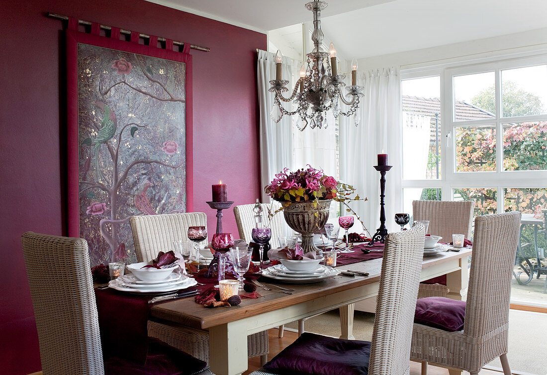 Festlich gedeckter Esstisch mit Rattanstühlen vor purpurfarbener Wand mit Wandbehang