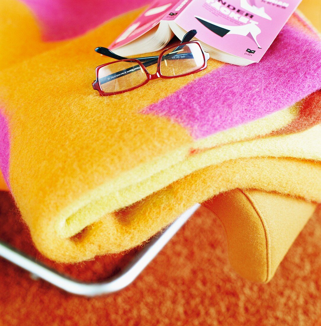 Glasses next to an open book and colorful throw blanket