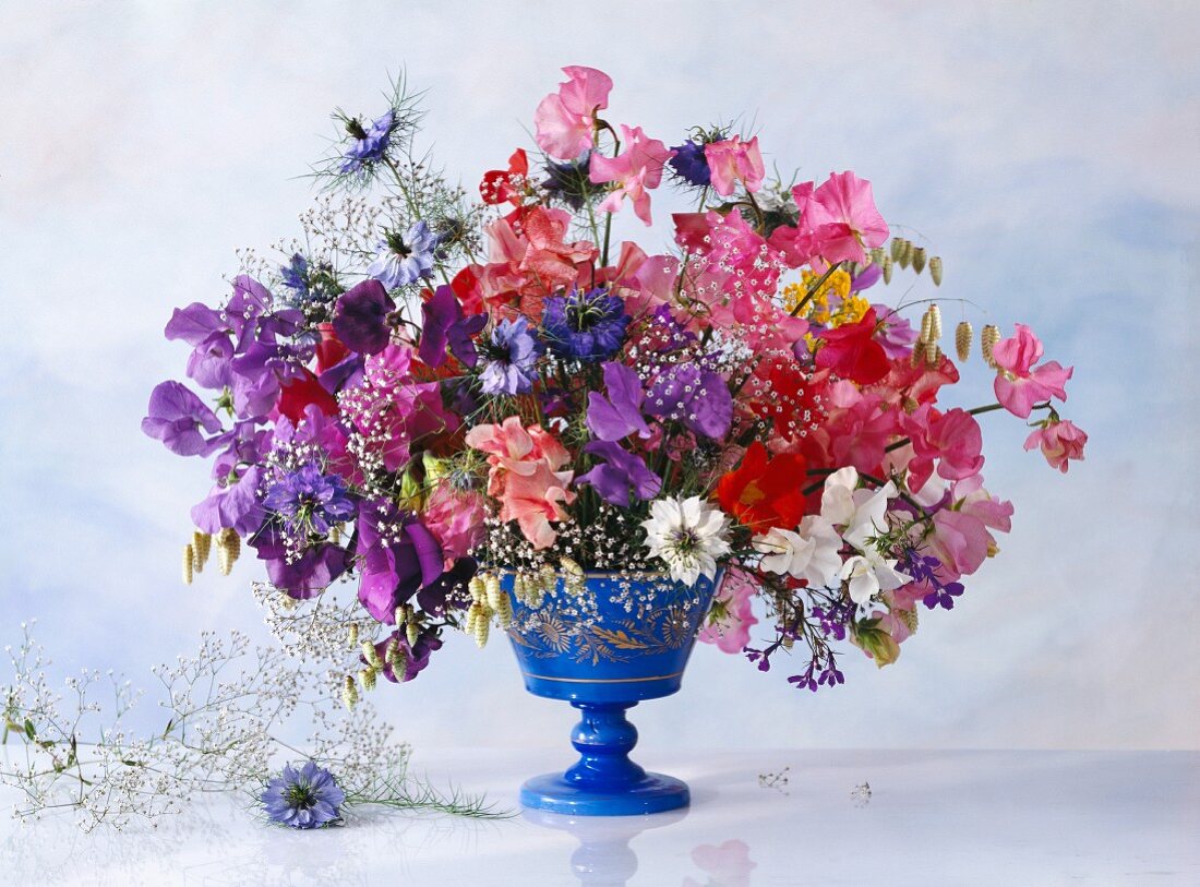 Bunter Frühlingsstrauss in blauer Vase vor heller gewolkter Wand