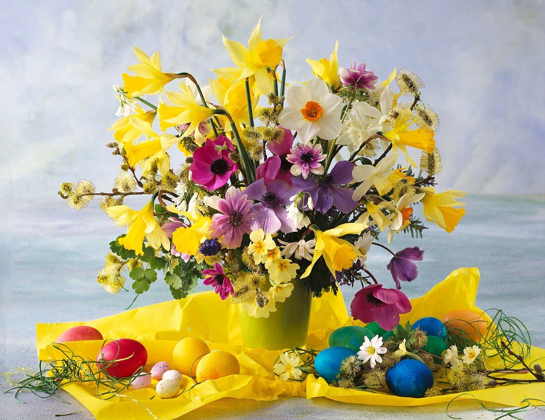 Bunter Blumenstrauss mit Narzissen und Osterschmuck auf gelbem Papier