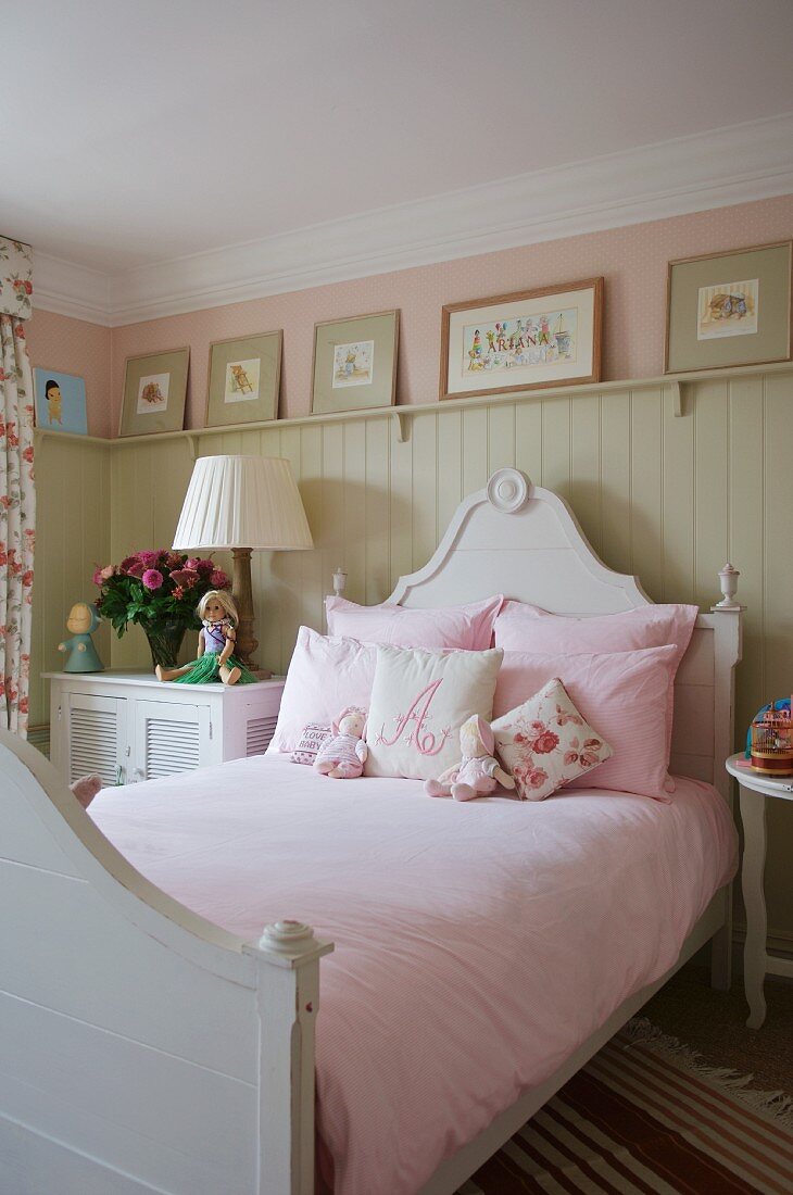Bett mit geschwungenem Kopfteil und rosa Bettwäsche vor hellgrauer Holzwand