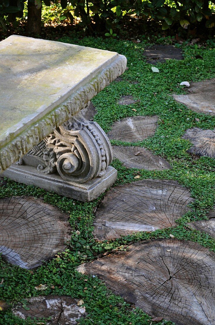 Antike Steinbank im Garten mit Trittstufen aus Baumscheiben