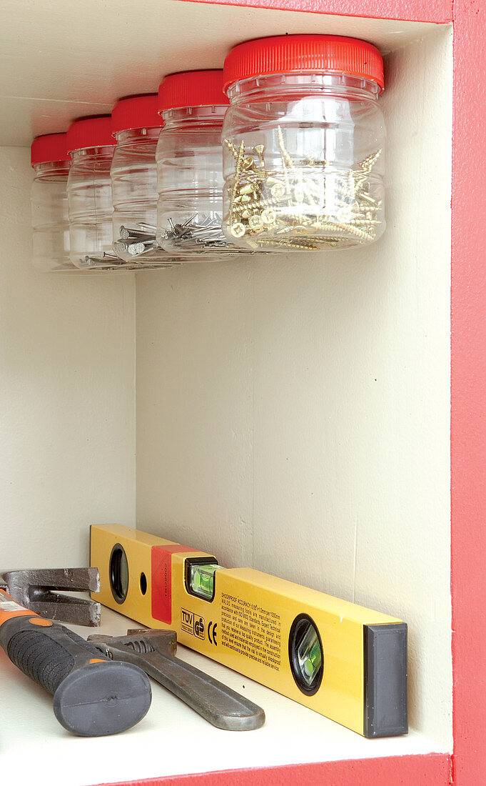 Tools in shelf compartment with plastic jars of nails and screws attached to upper shelf by lids
