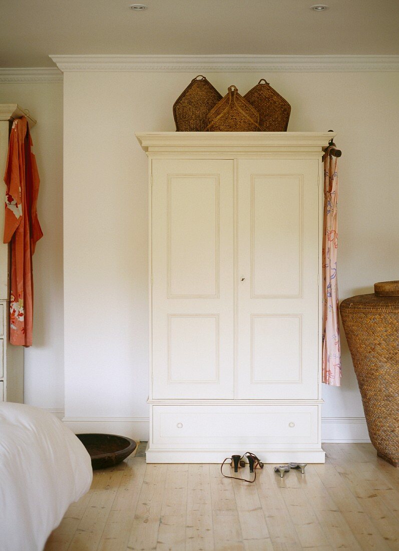 Wicker baskets on white-painted rustic wardrobe in plain bedroom