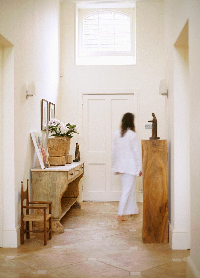 Woman walking down hallway with rustic wooden furniture